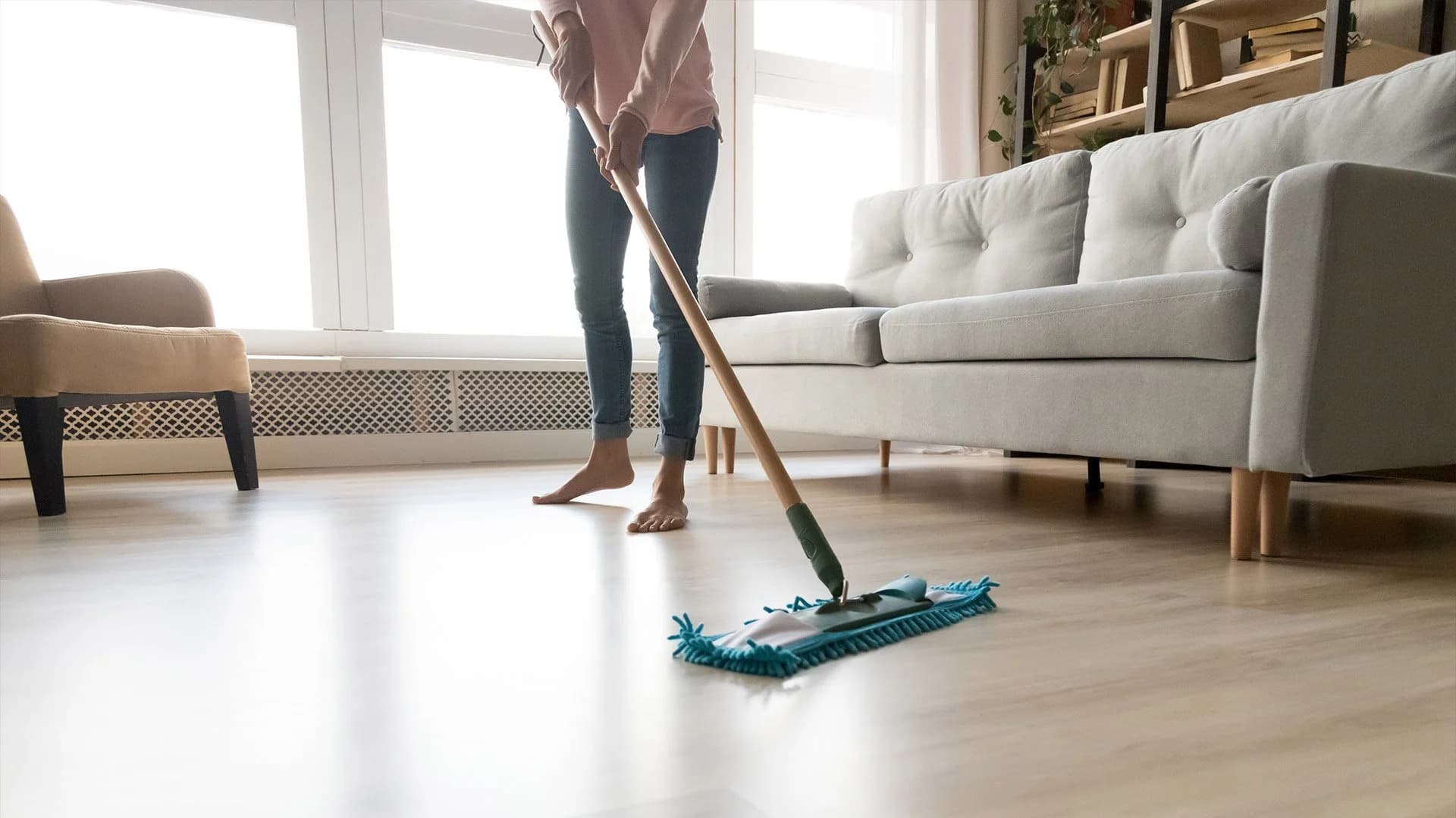 Cleaner mopping the wooden floor of a bright short-let apartment living room